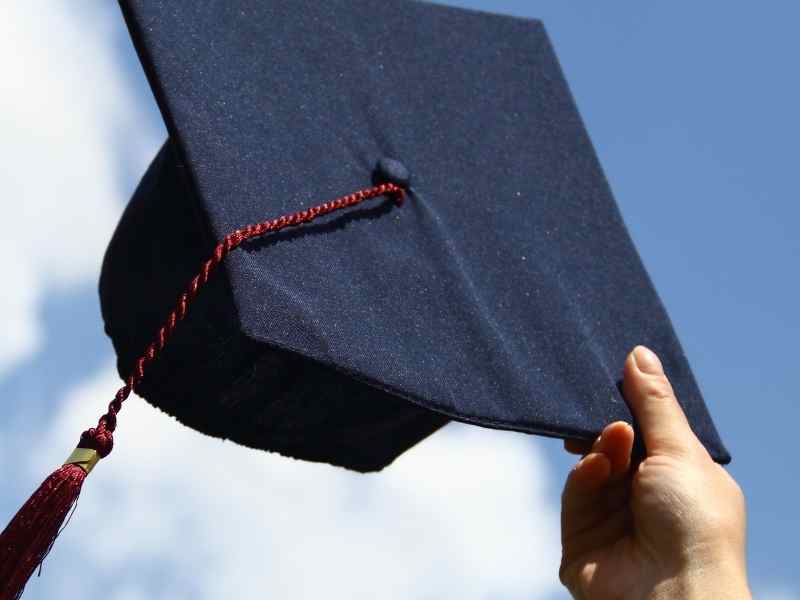 Mano sosteniendo un birrete de graduación contra el cielo, símbolo del paso de la educación al primer empleo formal y la movilidad social.