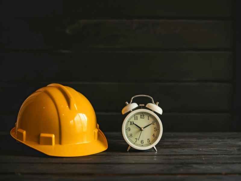 Casco de seguridad junto a un reloj, simbolizando jornada laboral y control de horarios.
