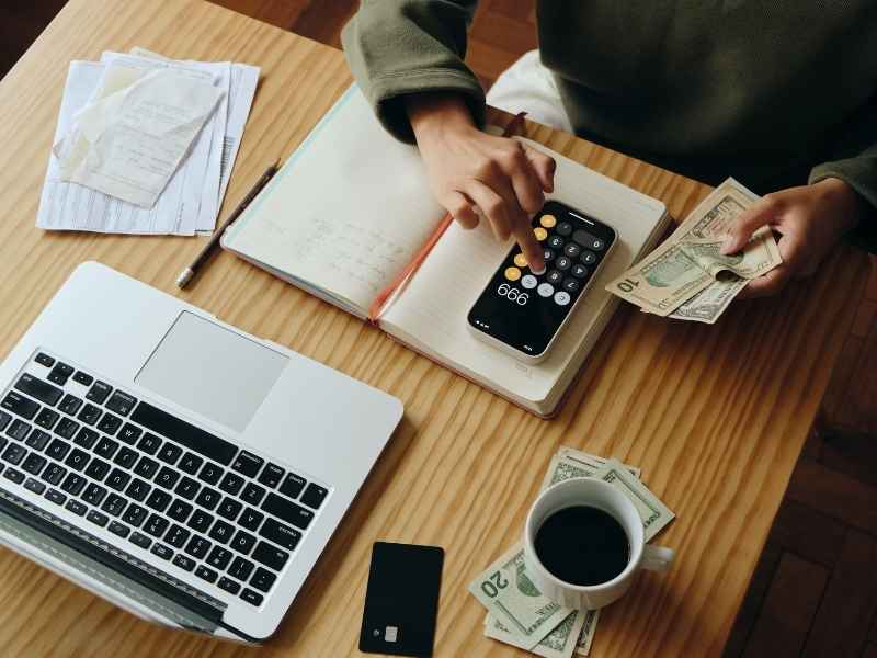 Persona calculando dinero y gastos con calculadora y libreta, representando planificación financiera.