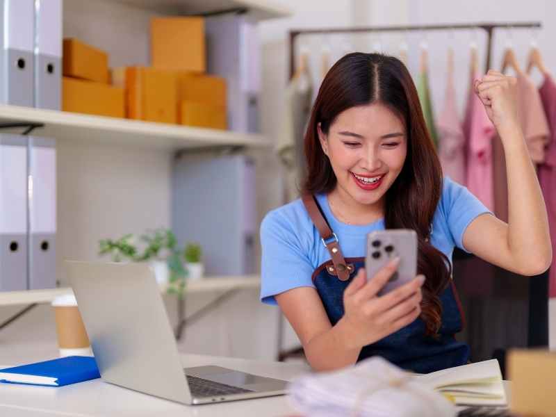 Emprendedora gestionando cobros y ventas desde el celular junto a su laptop, reforzando control de caja e impuestos en una pyme.
