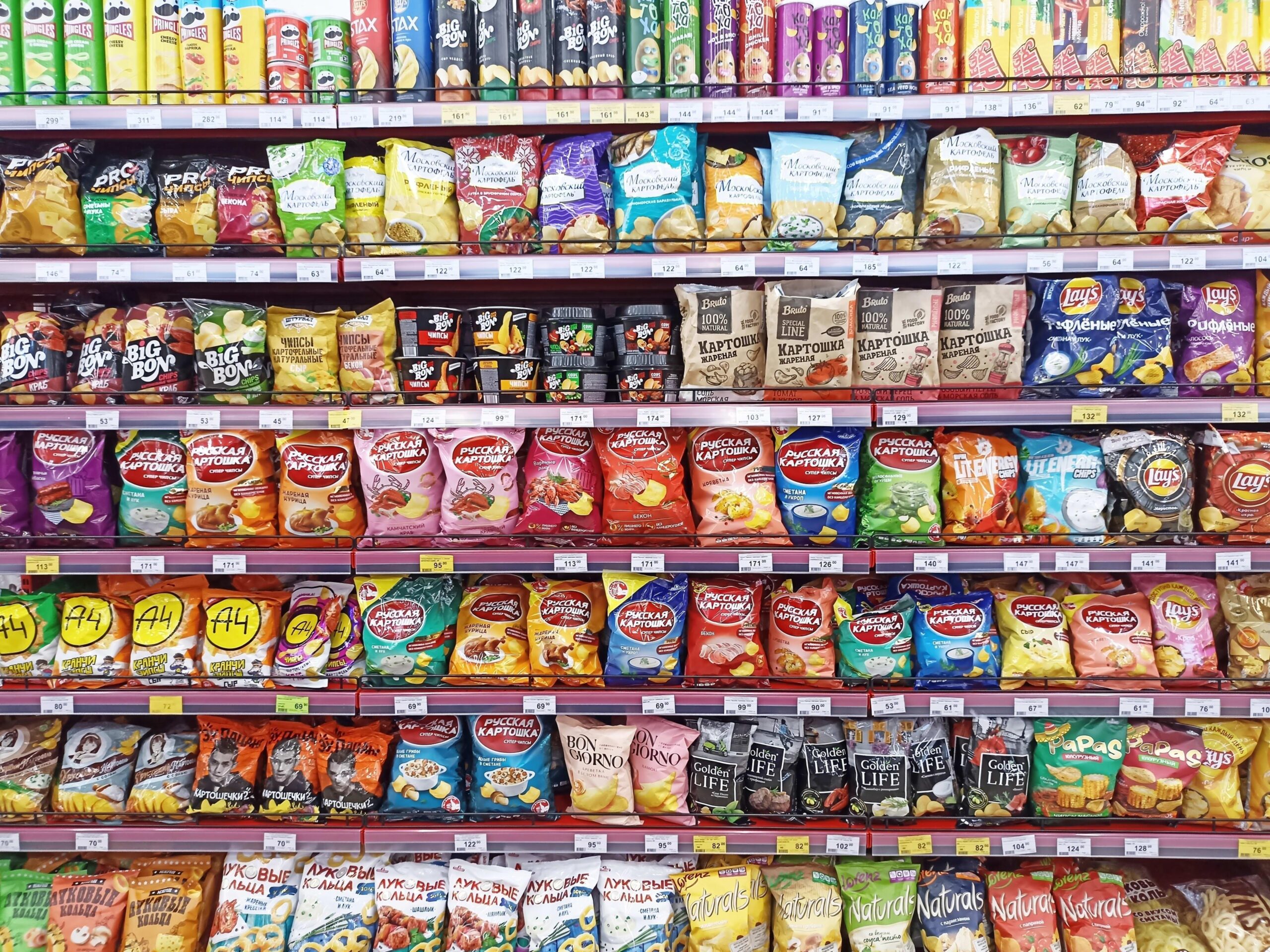 Estantes de supermercado con bolsas de papas fritas y otros snacks envasados en diferentes tamaños y presentaciones.