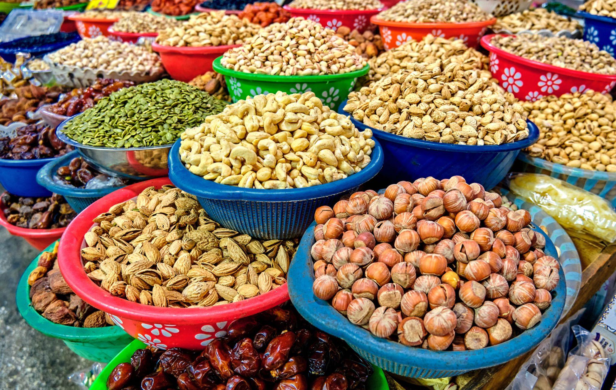 Puesto de mercado tradicional con recipientes de frutos secos, semillas y frutas deshidratadas disponibles para su venta.